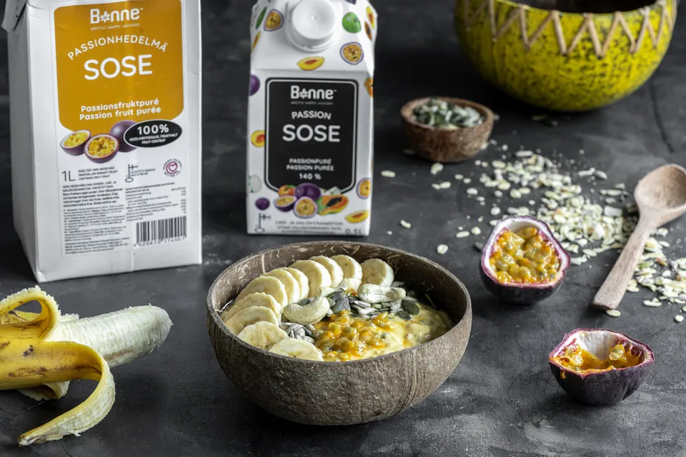 Two Bonne purée cartons beside a smoothie bowl in a coconut shell, with banana slices and halved passion fruit