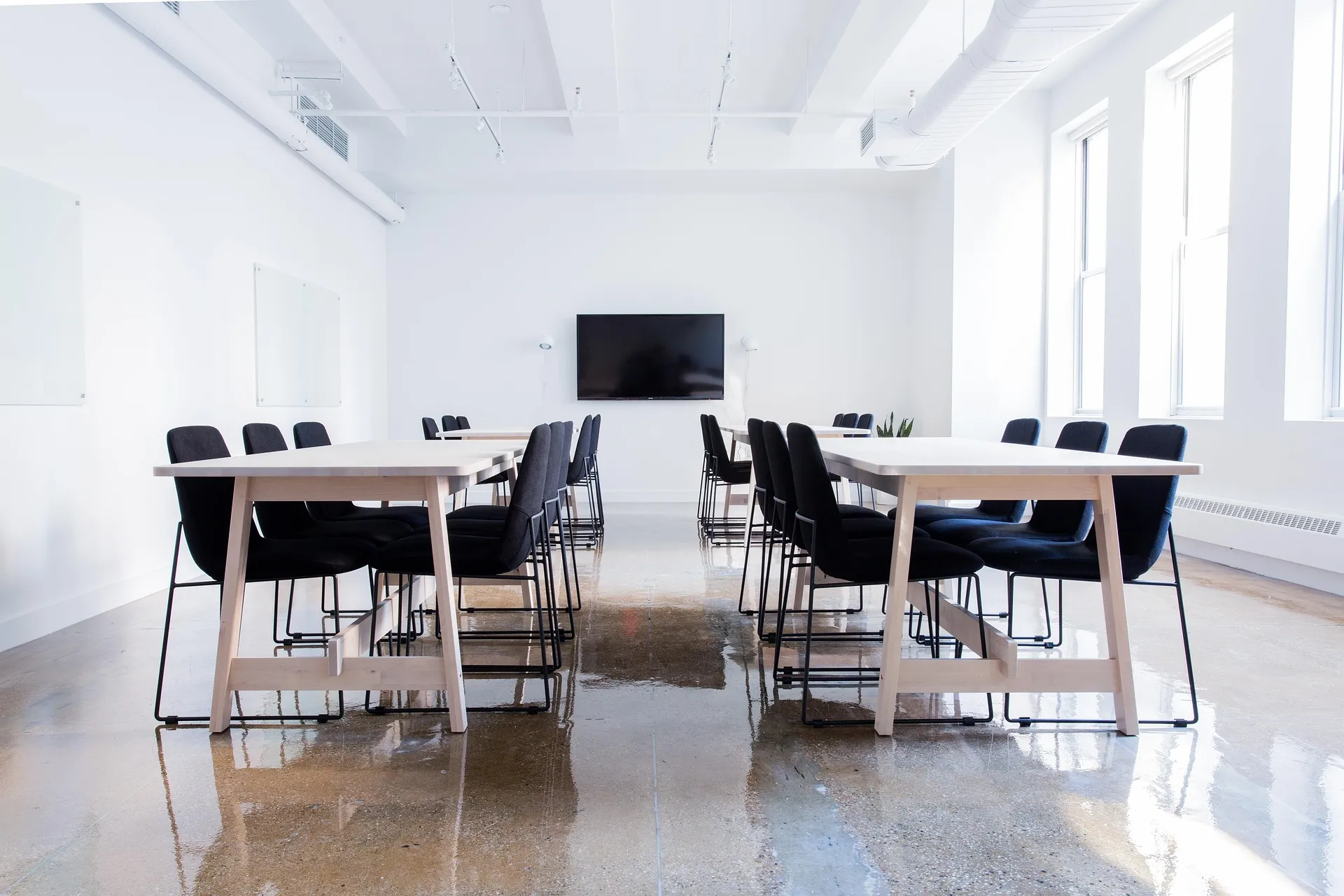 An empty seminar room with two long tables, black chairs and a blank screen